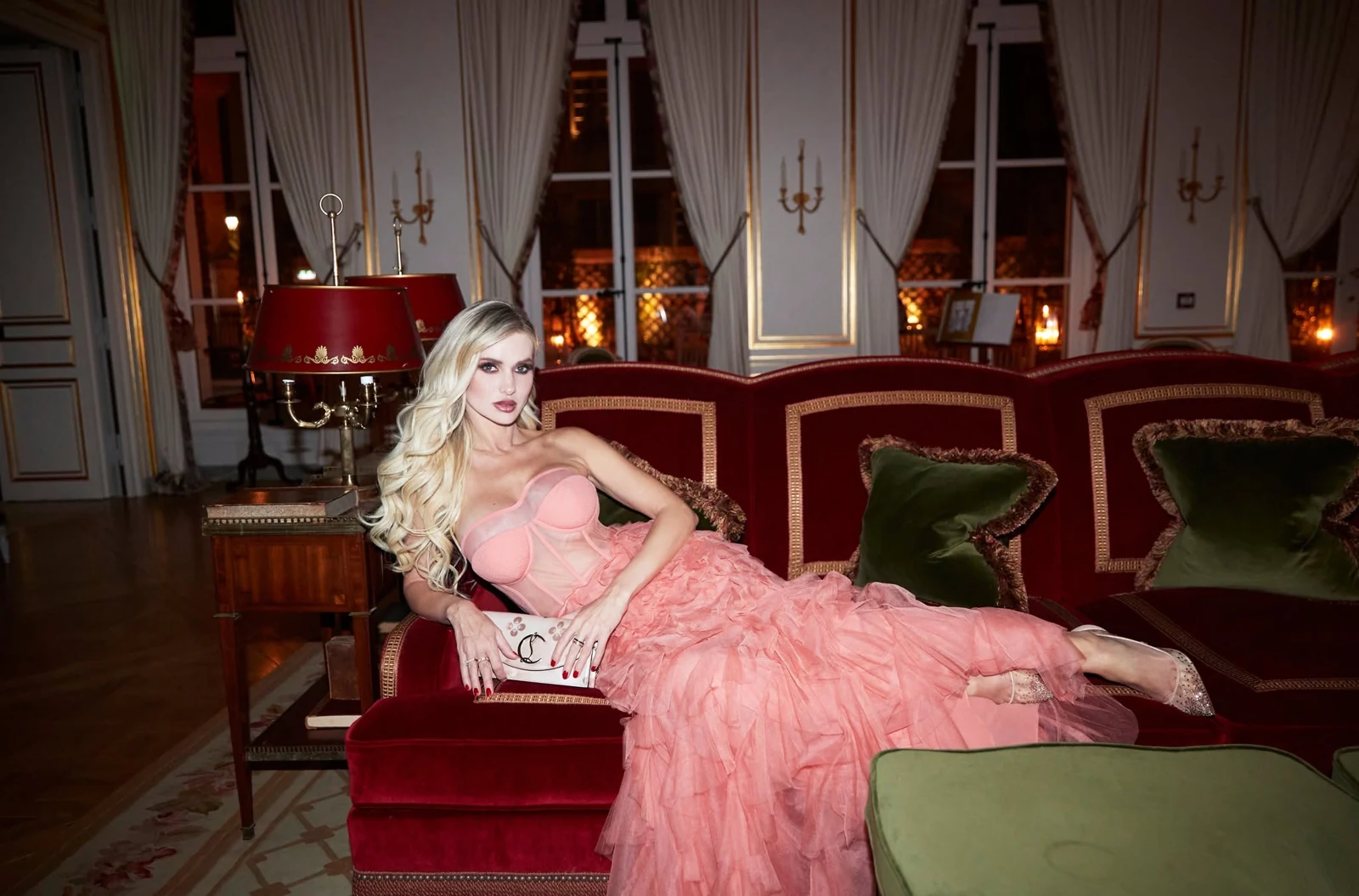 A client in a pink gown on a red velvet sofa, wearing long blonde waves